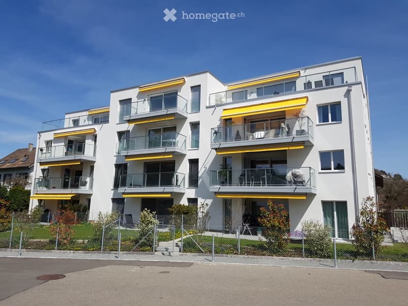 Modern multi-story apartment building with white facade, yellow accents, and multiple balconies.