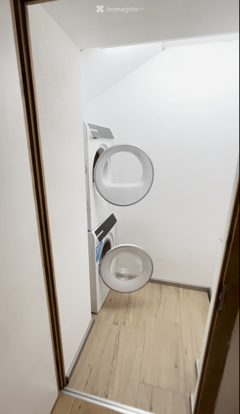 Empty room with wooden flooring and white walls, featuring a private washing machine in the corner.