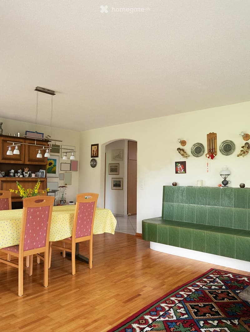 Dining room with wooden floor, dining table with chairs, green bench, and wall decorations.