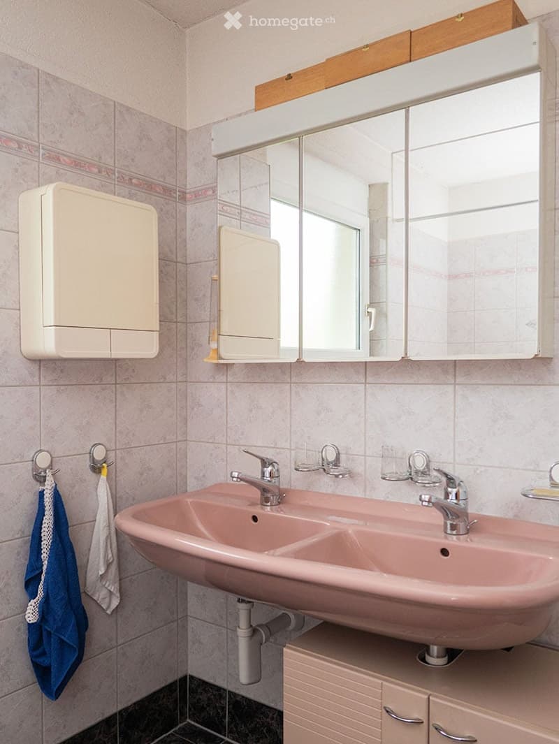 A bathroom with a double sink, a large mirror with cabinets above, and a towel hanging on a rack.