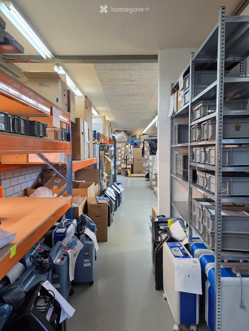 A long, well-lit corridor with metal shelving units on both sides, filled with cardboard boxes, storage bins, and various equipment.