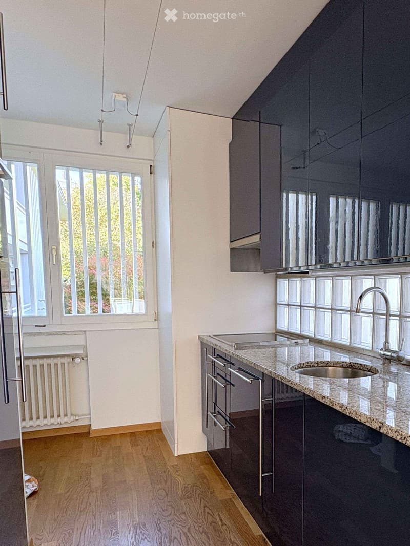 Modern kitchen with dark cabinets, granite countertop, stainless steel sink, and a window with a view of greenery.