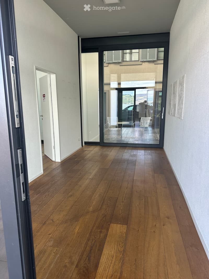Empty hallway with wooden flooring, white walls, and a large glass door leading to an outdoor area.