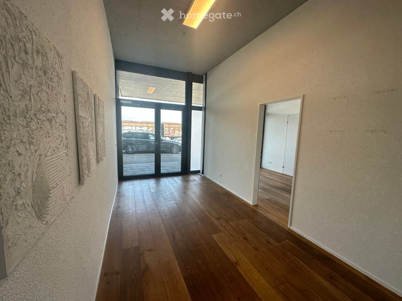 Empty hallway with wooden flooring, large glass doors leading outside, and a textured wall art piece on the left side.