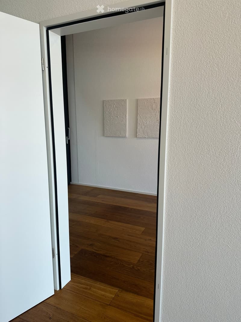 Empty room with wooden flooring and white walls, featuring two decorative wall pieces.