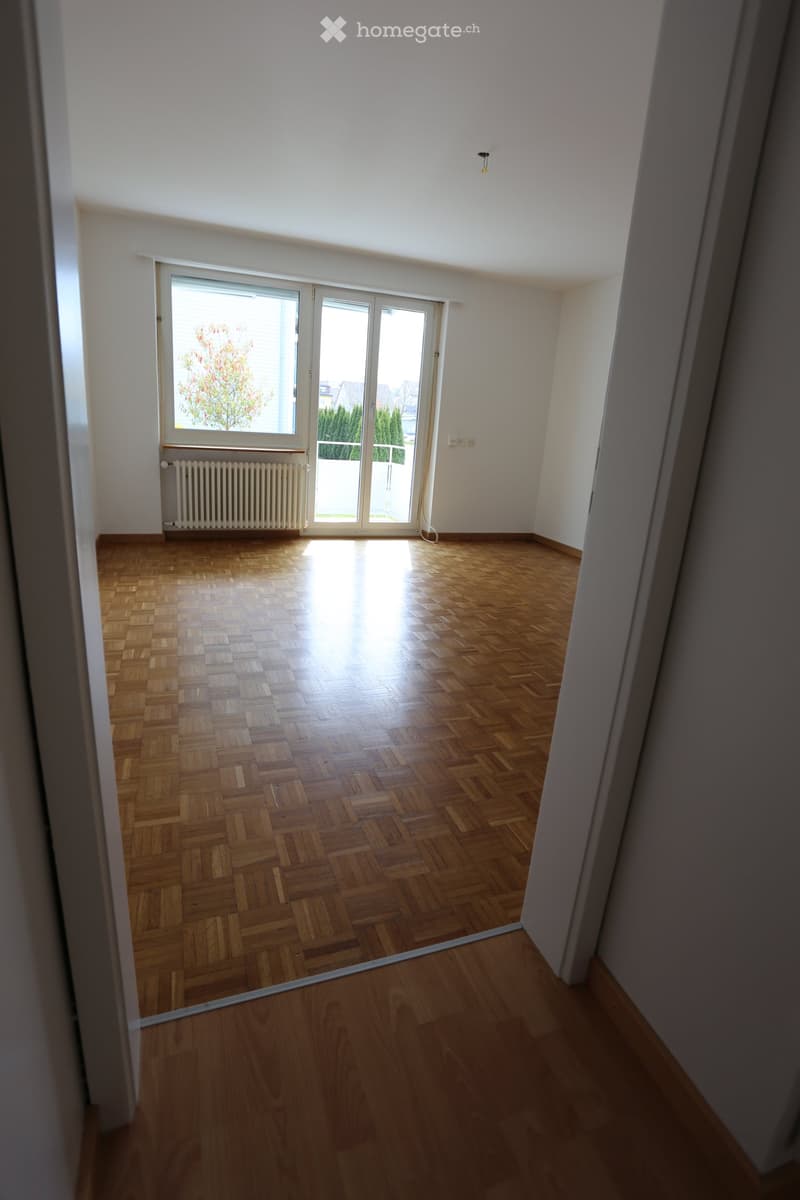 Empty room with wooden flooring, large window with sliding doors, radiator, and visible light fixture on the ceiling.
