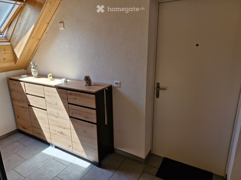 A small, well-lit room with a wooden cabinet, a small table with decorative items, and a door leading out.