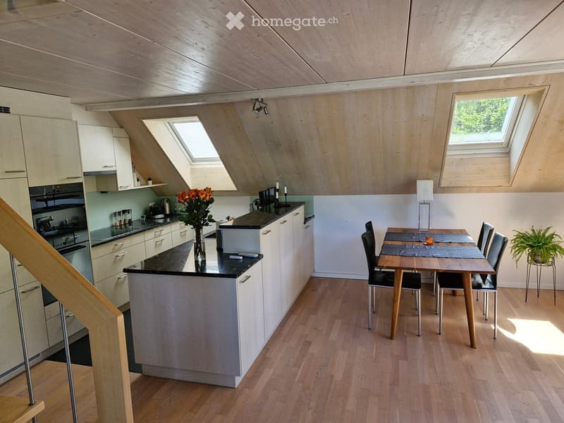 Modern kitchen and dining area with light wood cabinets, black countertops, a central island, and a dining table with chairs. The space features skylights and a wooden ceiling.