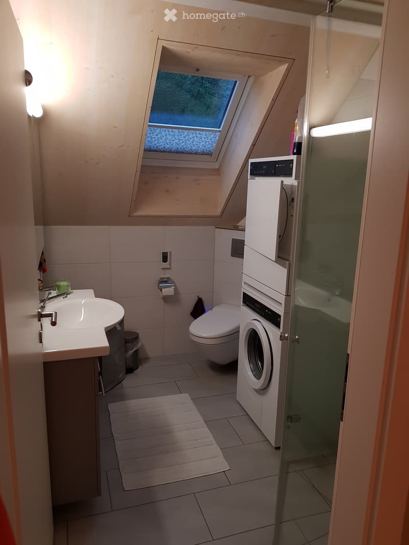 Modern bathroom with a skylight window, white tiles, a sink, toilet, washing machine, and a small shower area.