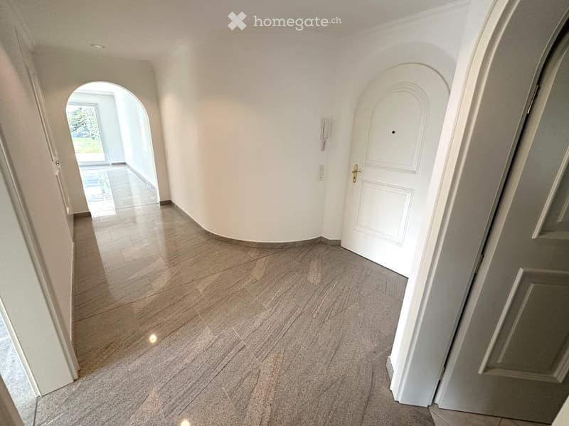 A clean, modern hallway with polished tile flooring, white walls, and arched doorways leading to other rooms.