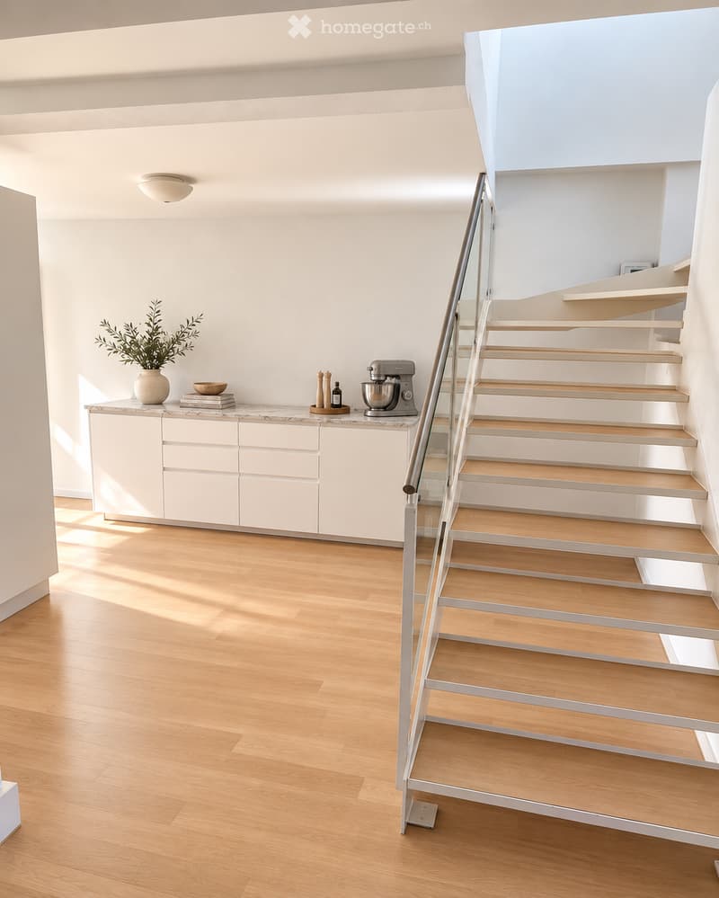 Modern, minimalist room with light wooden flooring, white cabinetry, and a staircase with wooden steps and a glass railing. A vase with greenery, a bowl, books, and a mixer are placed on the cabinet.