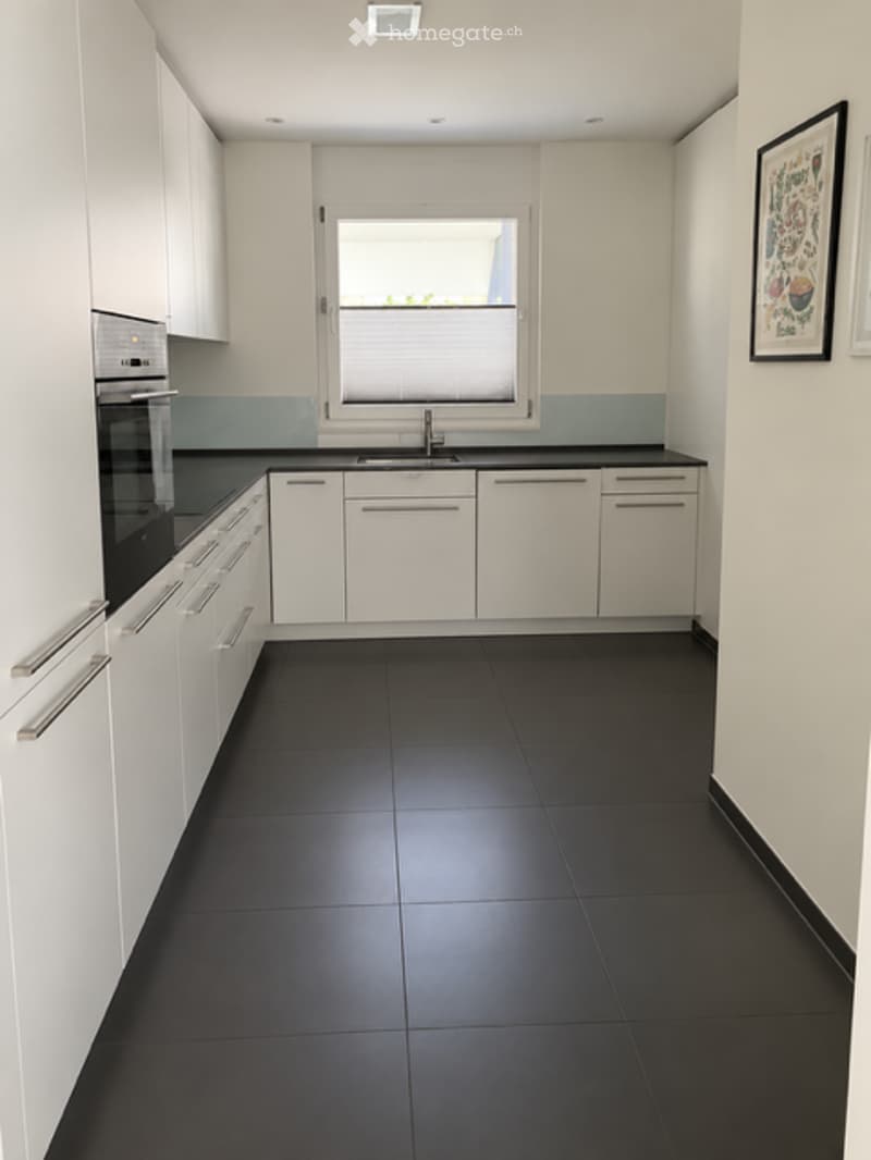 Modern kitchen with white cabinets, black countertops, and black tiled floor. Features a window with blinds, a sink with a faucet, and an oven.