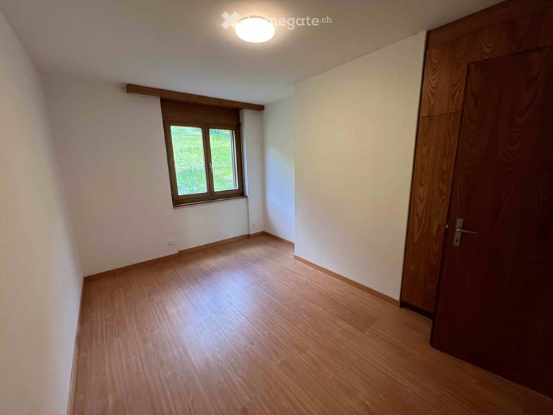 Empty room with wooden flooring, white walls, a single window, and a closed wooden door.