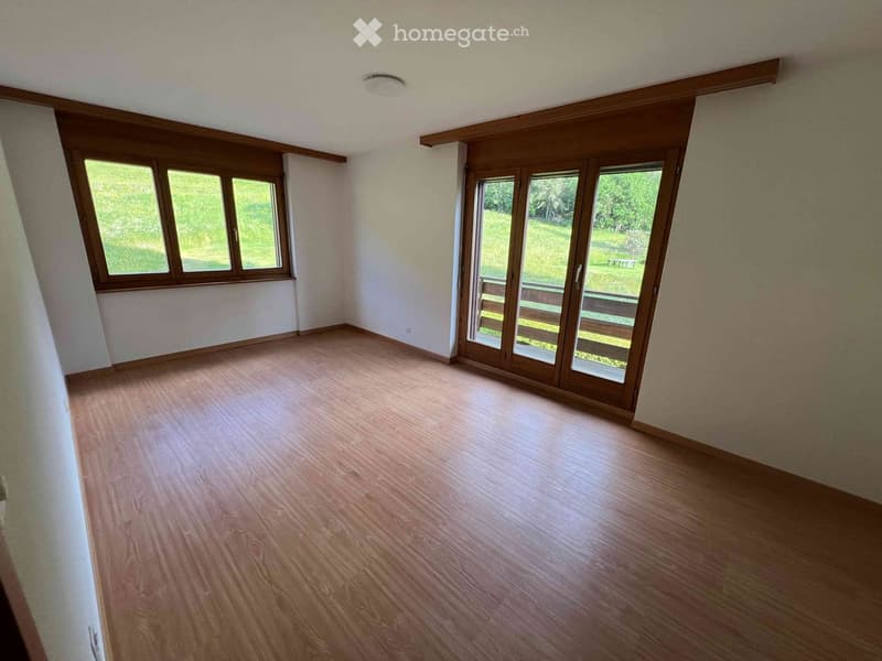 Empty room with wooden flooring, large windows, and sliding glass doors leading to an outdoor area.