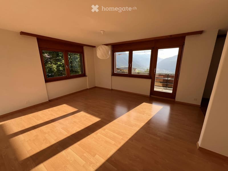 Empty room with wooden flooring, large windows, and a sliding glass door leading to a balcony. Natural light illuminates the space.