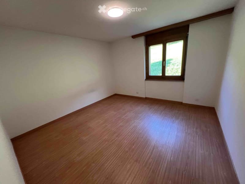 Empty room with wooden flooring, white walls, and a single window with wooden frame. The ceiling has a recessed light fixture.