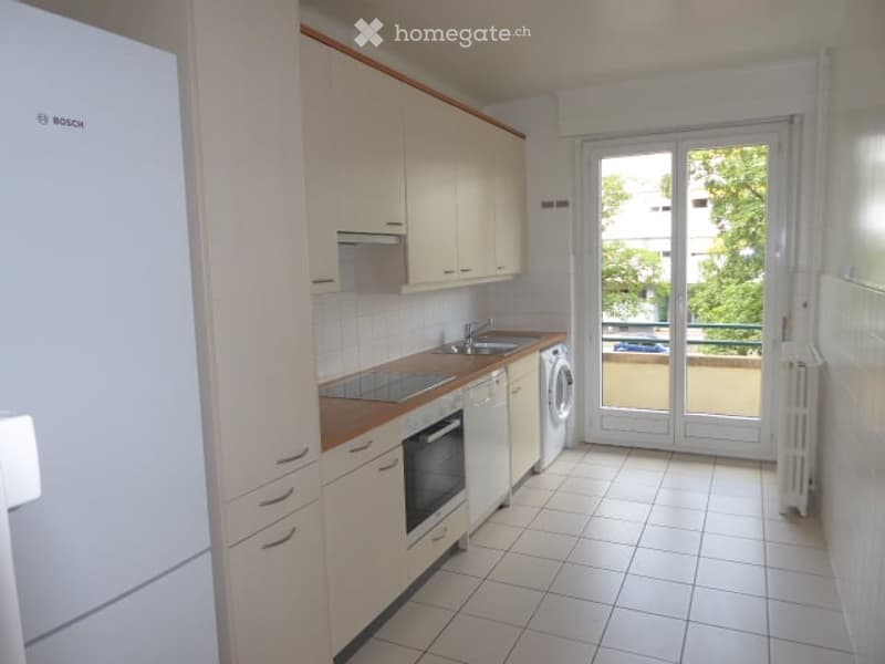 Modern kitchen with white cabinets, tiled floor, stainless steel sink, dishwasher, oven, and washing machine. Large window with balcony access.