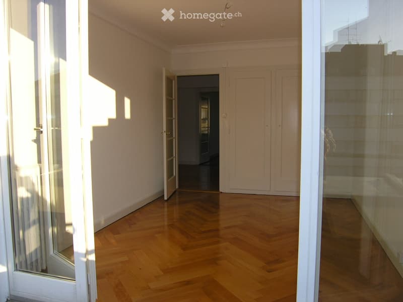 Empty room with wooden flooring, white walls, and large glass doors leading to a balcony.