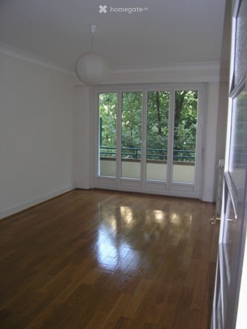 Empty room with wooden flooring, white walls, large glass doors leading to a balcony, and a hanging light fixture.