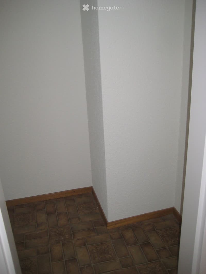 Empty room with brown tiled floor and white walls, featuring a wooden baseboard trim.
