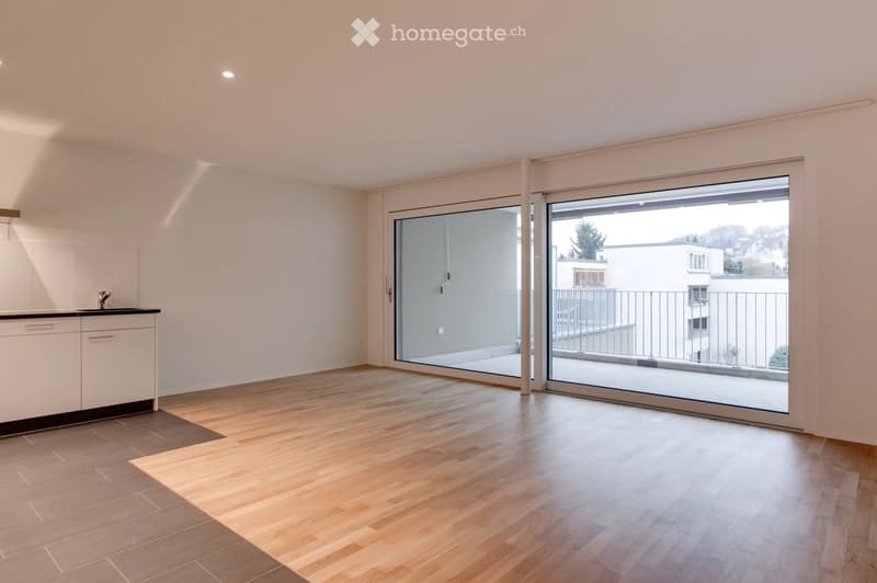 Empty room with light wooden flooring, white walls, and large sliding glass doors leading to a balcony.