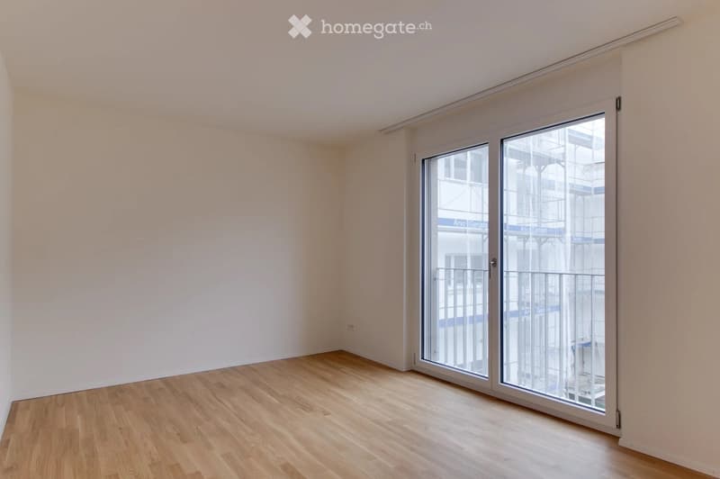 Empty room with light wooden flooring and white walls, featuring a large sliding glass door leading to a balcony.