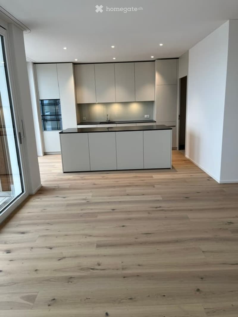 Empty kitchen with light wood flooring, white cabinetry, and a central island with black countertops.