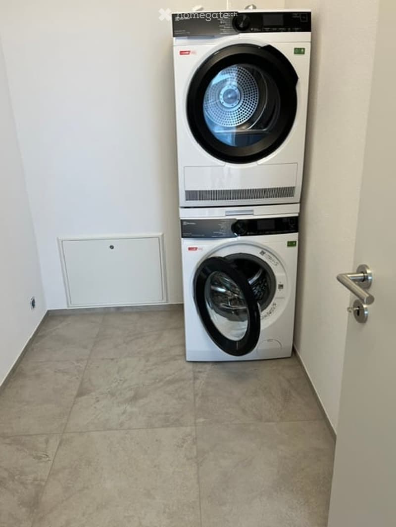 Empty room with tiled floor and white walls, featuring a stacked washer and dryer unit against the wall.