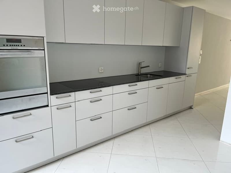 Modern kitchen with white cabinets, black countertops, and stainless steel appliances including an oven and sink.