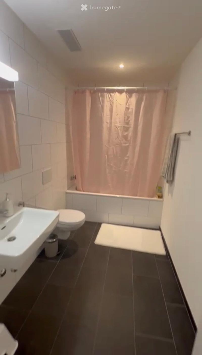Modern bathroom with black tiled floor, white sink, toilet, bathtub, and shower curtain. Includes a white towel and a small trash can.