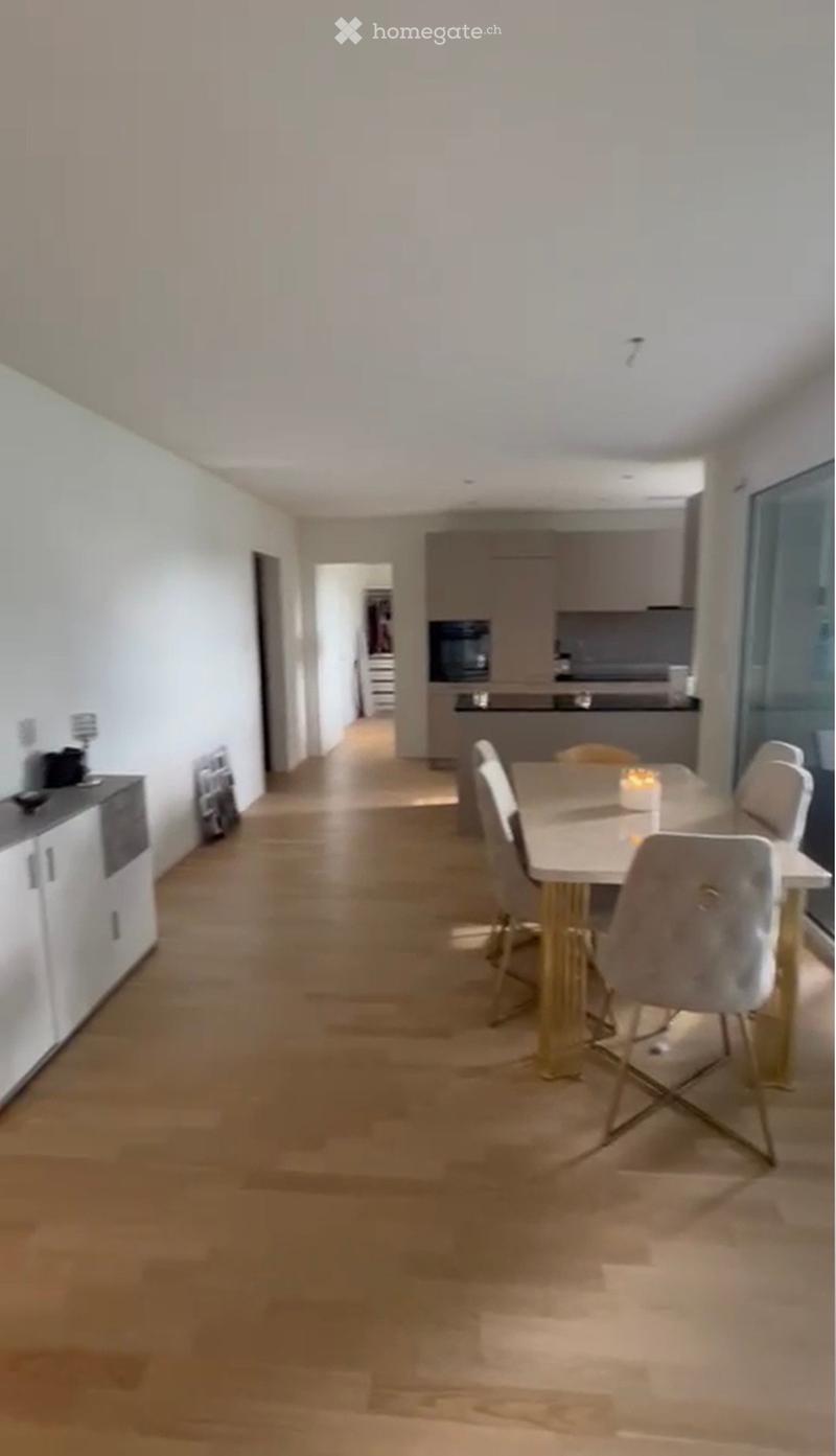 Modern dining area with a white dining table, four chairs, and a microwave in the adjacent kitchen area.