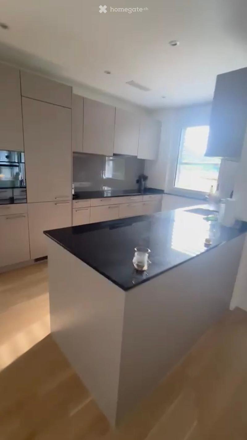 Modern kitchen with white cabinets, black countertop, and a central island. Features a sink, faucet, and a single cup on the counter.