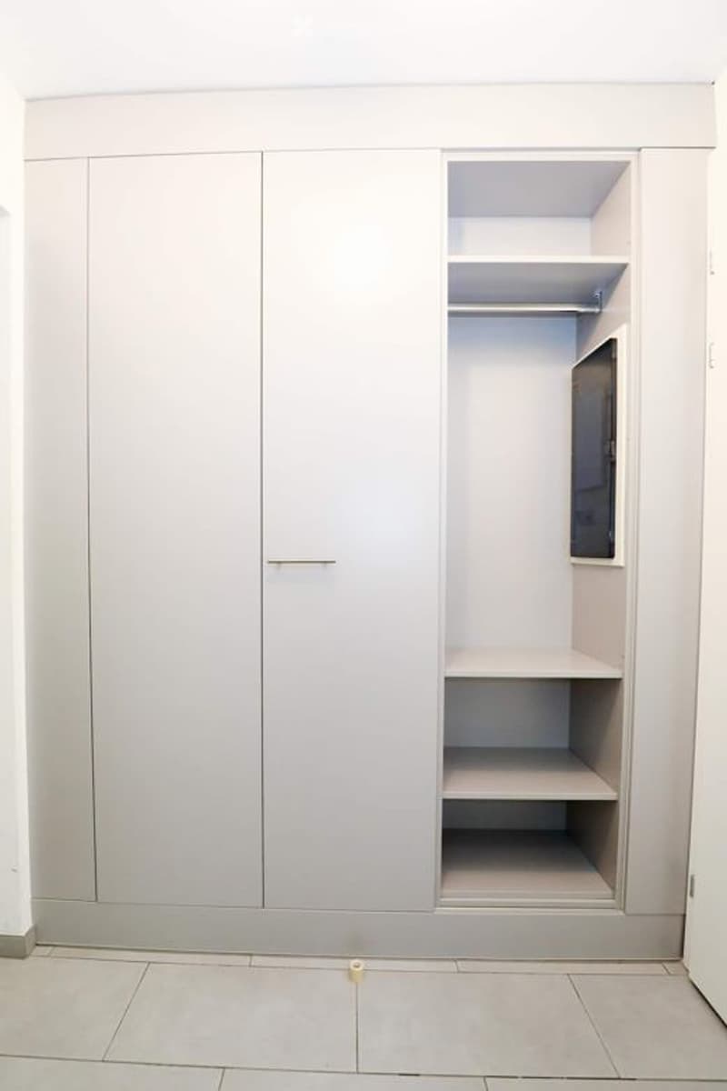 Empty room with built-in white closet and shelving unit, light grey tiled floor, and white walls.
