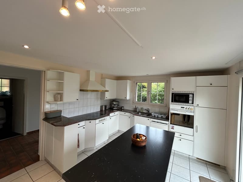 Modern kitchen with white cabinets, black countertops, and stainless steel appliances including a refrigerator, microwave, oven, and dishwasher. A bowl of fruit is placed on the island.