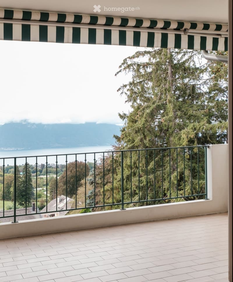 Balcony with white tiled floor, green metal railing, and scenic view of mountains and lake.