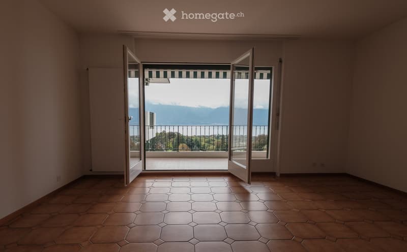 Empty room with hexagonal tile flooring, large open sliding doors leading to a balcony with a scenic mountain view.