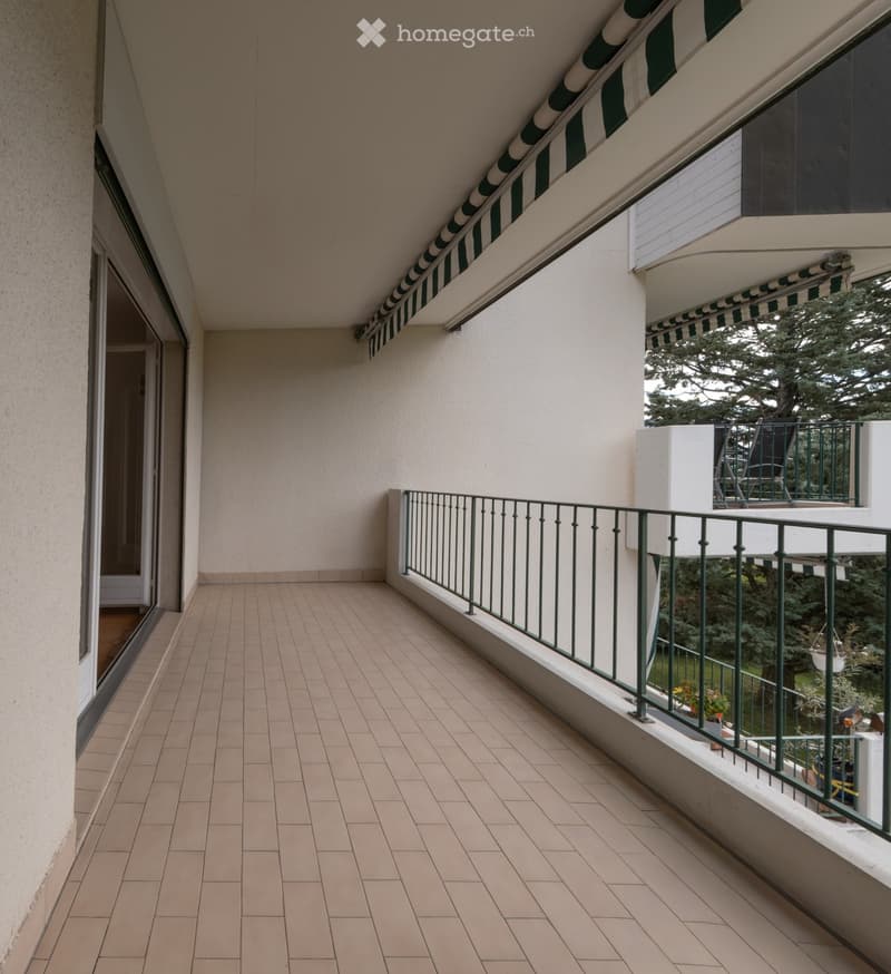 Balcony with tiled floor, metal railing, and striped awning. Adjacent balcony visible with outdoor furniture.