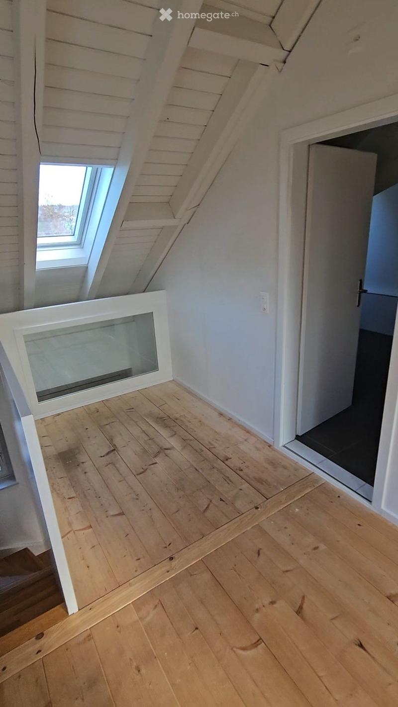 Empty attic space with wooden flooring, white walls, and a skylight window. No furniture or equipment present.