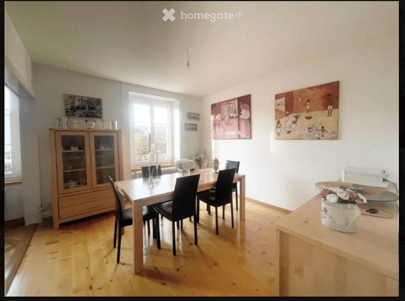 Bright dining room with wooden flooring, large windows offering a scenic view, a wooden dining table surrounded by black chairs, a wooden cabinet with glass doors, and decorative vases on the table and counter.