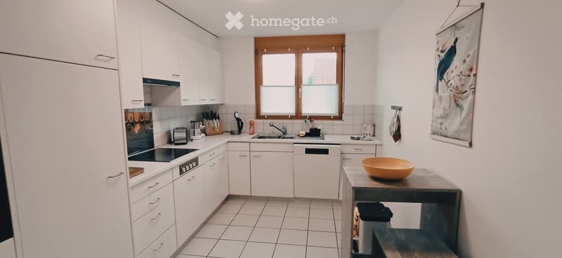 Modern kitchen with white cabinets, stainless steel appliances, and a central island. Features a sink, stove, oven, and a small table with a bowl on it.