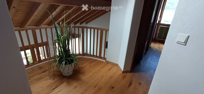 Wooden staircase with a railing, light-colored walls, and a potted plant on the landing.