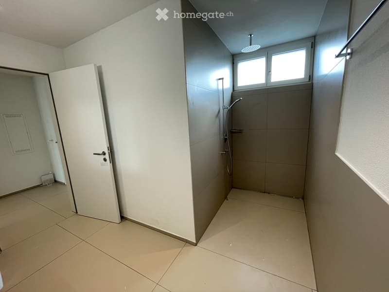 Empty bathroom with shower, tiles on the floor and walls, small window, and a door.
