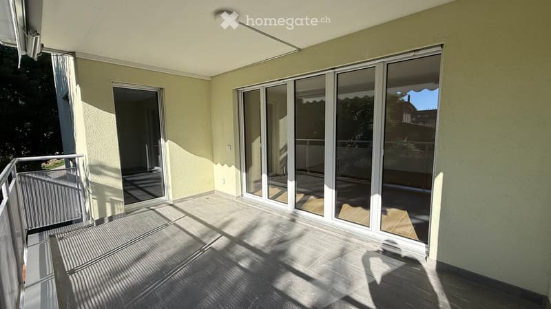 Balcony with large sliding glass doors, tiled floor, metal railing, and a view of greenery.