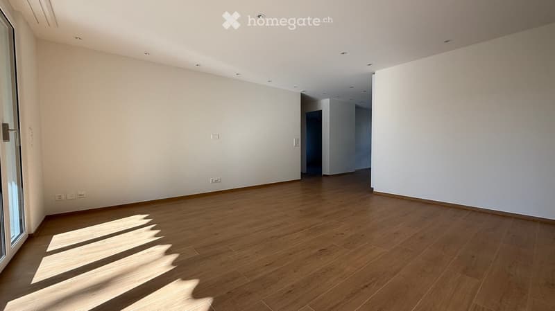 Empty room with wooden flooring and white walls, featuring recessed ceiling lights and a large window with blinds.