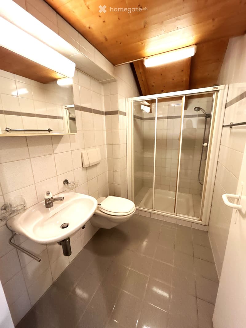 Modern bathroom with white tiles, a sink, toilet, mirror, and a glass-enclosed shower area.