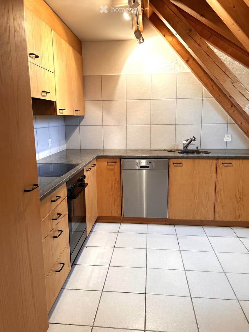 Modern kitchen with light wooden cabinets, stainless steel appliances, and tiled countertops.