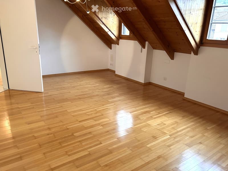 Empty attic room with wooden flooring, white walls, and skylight windows.