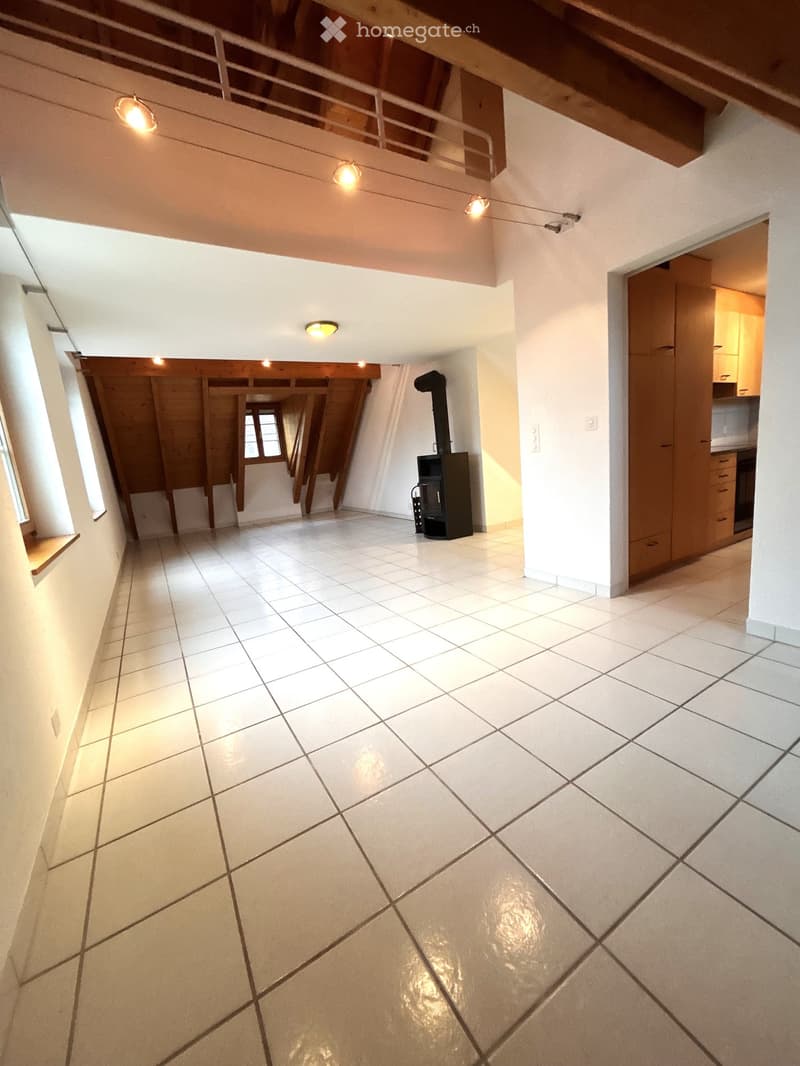 Empty room with white tiled floor, exposed wooden beams, and built-in cabinets. Features a wood-burning stove and a small window with a view of the outside.