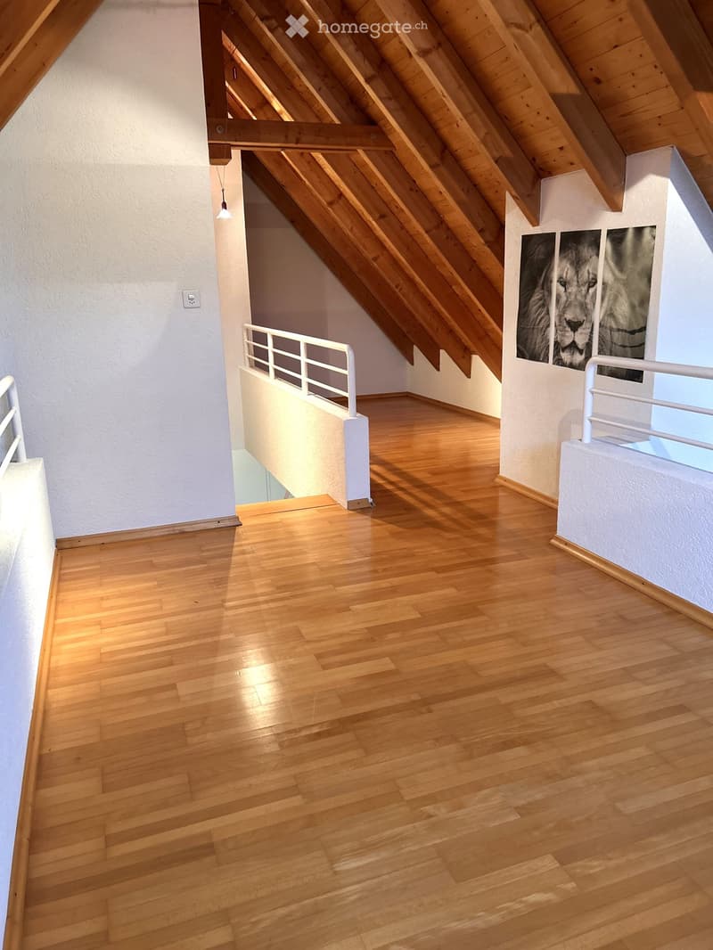 Empty attic space with wooden flooring, white walls, exposed wooden beams, and a staircase leading downwards.