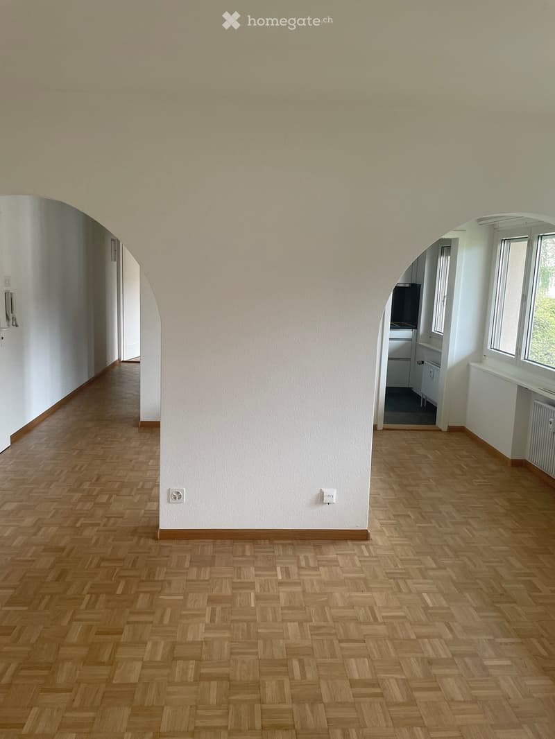 Empty hallway with wooden herringbone flooring, white walls, and arched doorways leading to adjacent rooms.